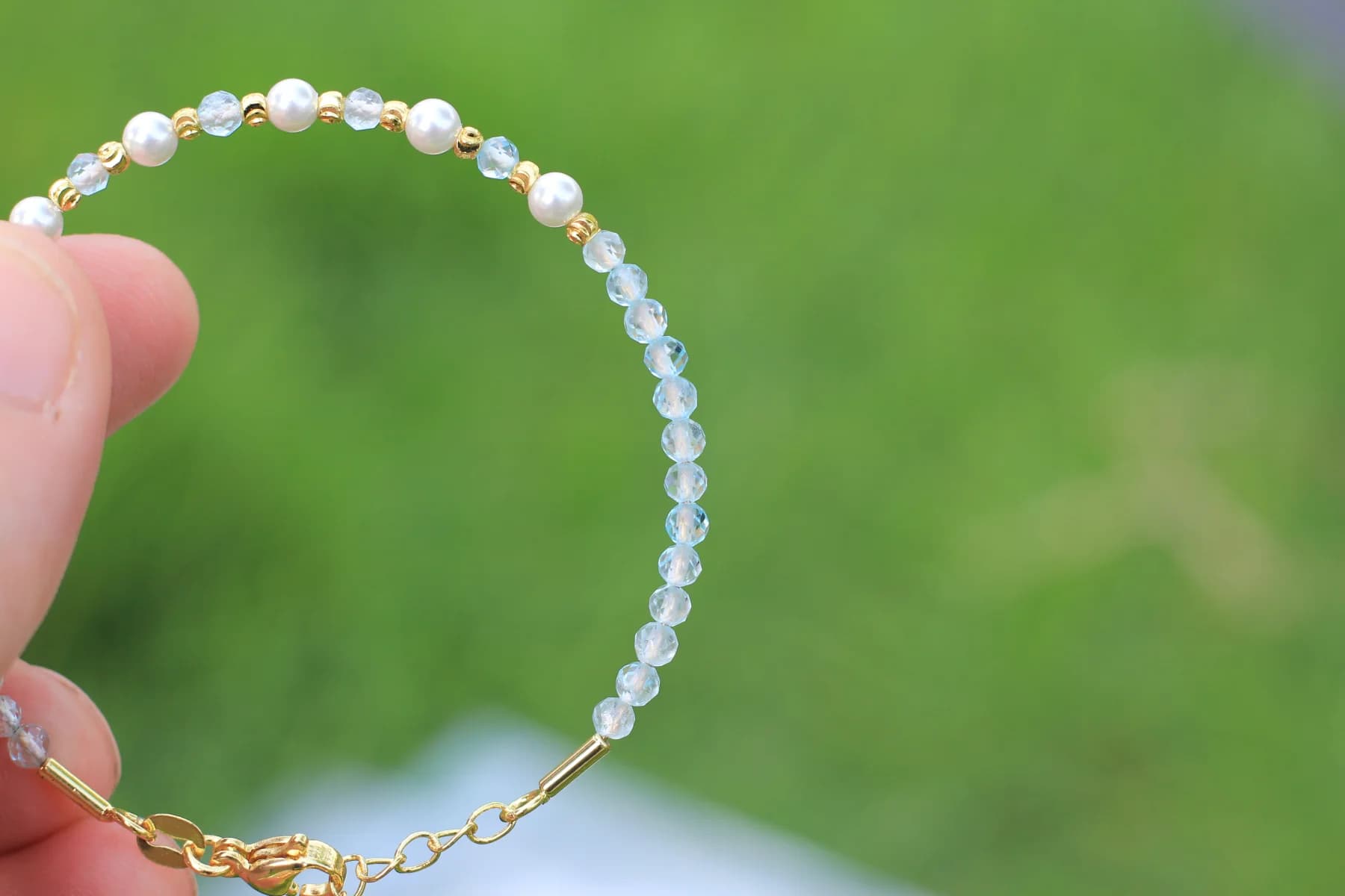 Blue topaz and mother-of-pearl bracelet held against a green outdoor background